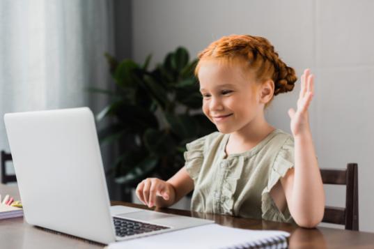 young girl sitting in front of a computer waving at someone on a video call