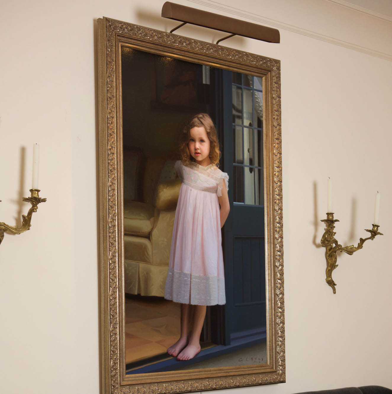 Painted portrait of a young girl in a pink dress with an ornate gold frame and light above.